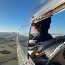 Alumno piloteando un planeador sobre los campos, visto desde la cabina