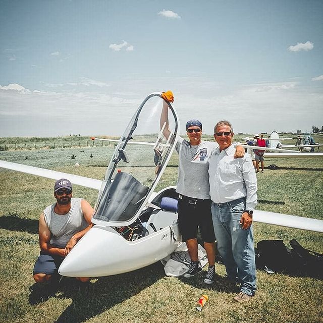 Tres pilotos junto a un planeador en la pista