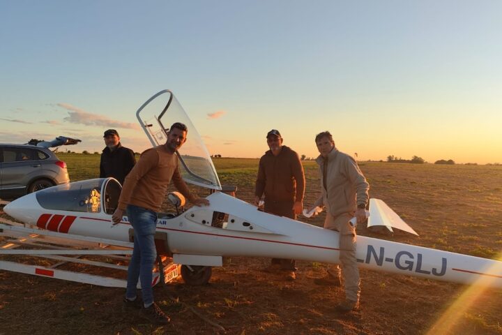 Pilotos junto a un planeador en la pista al atardecer