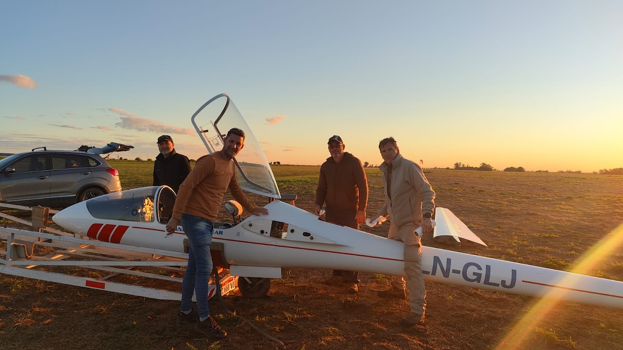 Pilotos junto a un planeador en la pista al atardecer